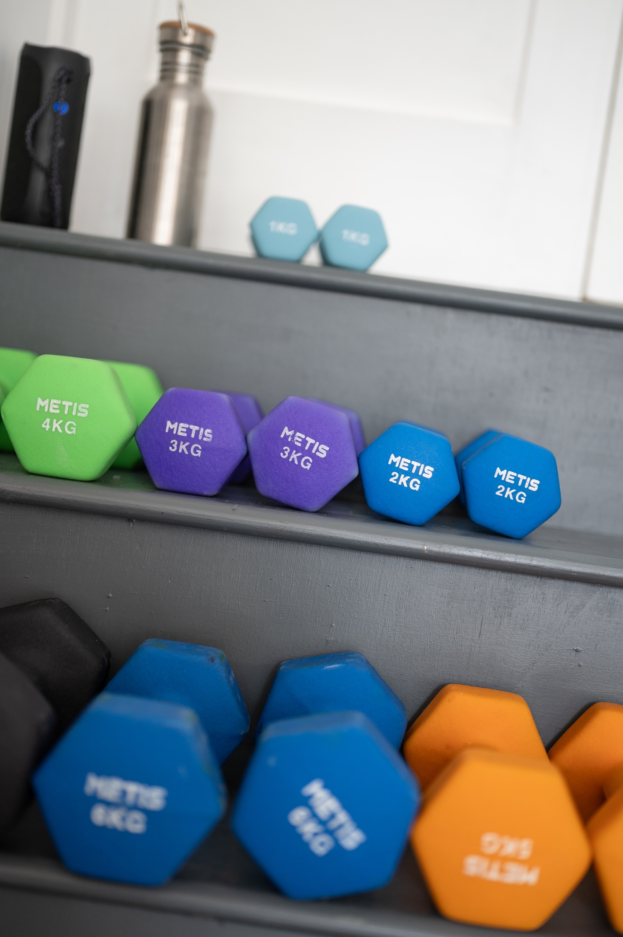 A rack of coloured hex dumbbells on grey shelving in Tanya's studio